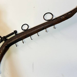 May include: A wooden ox yoke with metal rings and hooks. The yoke is brown and has a silver-colored metal ball on the end.