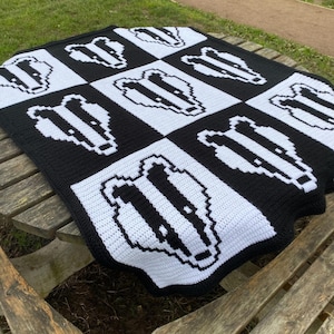 May include: A black and white crocheted blanket with a repeating pattern of badger faces. The blanket is made with a chunky yarn and has a soft, textured feel.