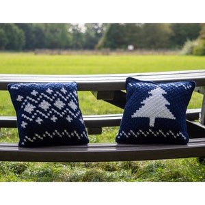 May include: Two blue and white crocheted throw pillows with winter holiday designs. One pillow features a snowflake pattern, and the other has a white Christmas tree.