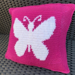 Könnte beinhalten: Ein rosa gehäkeltes Kissen mit einem weißen Schmetterlingsmuster.