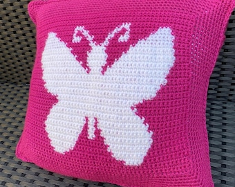 Op de afbeelding: Een roze gehaakt kussen met een wit vlindermotief.