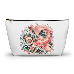May include: A white zipped pouch featuring a central graphic illustration of a pink and white koi fish swimming amidst stylised teal ocean waves, scattered pink cherry blossoms, and a single mahjong tile with a floral design.