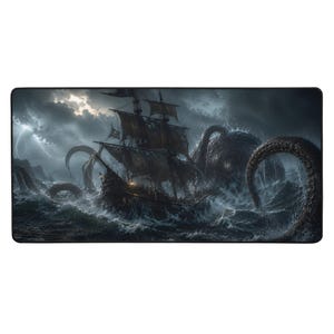 Op de afbeelding: Een rechthoekige bureaumat met een donkere, stormachtige oceaan-scène waarin een groot houten zeilschip wordt aangevallen door een reusachtige octopus met lange, getextureerde tentakels die uit de woelige golven onder een bewolkte lucht oprijzen.