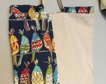 May include: A blue canvas tote bag with a white canvas pocket on the front. The tote bag has a colorful bird pattern on the front. The birds are on a wire and are all different colors and designs.