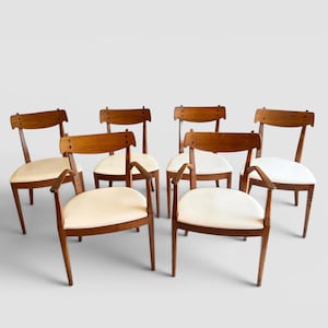 May include: A set of six wooden dining chairs with light-colored upholstered seats. Two chairs feature armrests, while four are armless. Each chair has a curved wooden backrest and four tapered legs, showcasing a consistent wood grain finish.