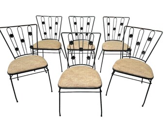 May include: Set of seven vintage metal dining chairs. Each chair has a black metal frame with a floral design on the backrest and a beige upholstered seat. The chairs are arranged against a white background.