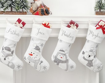 Puede incluir: Cuatro calcetines de Navidad blancos con diseños de animales grises y blancos y nombres personalizados: Arthur, Jace, Paisley y Meghan. Los calcetines están llenos de cajas de regalo rojas con cinta blanca.