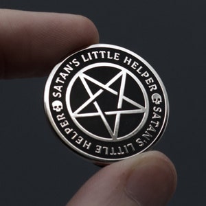 Könnte beinhalten: Eine silberne Anstecknadel mit einem schwarzen Pentagramm und dem Text "Satan's Little Helper & Satan's Little Helper" am Rand.
