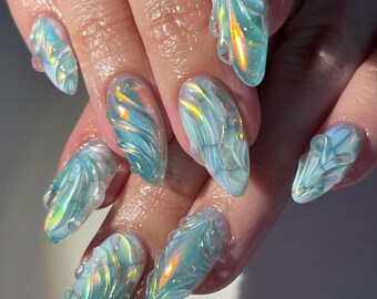 May include: Almond-shaped nails featuring a three-dimensional, translucent light blue gel design. The surface displays raised, swirling patterns with an iridescent, pearlescent finish that reflects gold and green light across the textured layers.