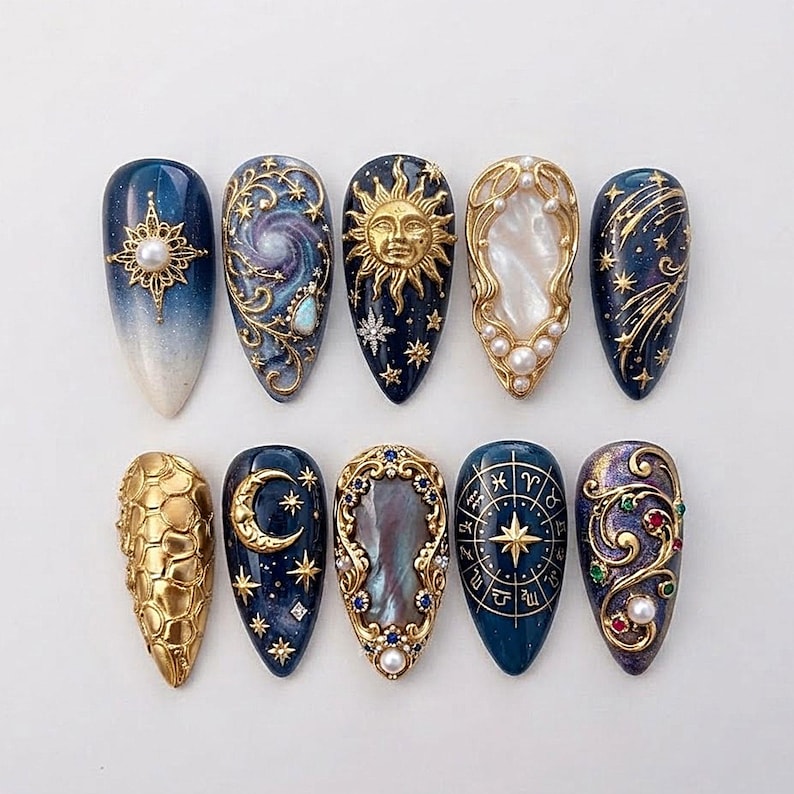 Op de afbeelding: Een set van tien amandelvormige press-on nagels met hemelse thema's. Ontwerpen bevatten gouden zonnen, manen, sterren, dierenriemwielen en sterrenstelsels op donkerblauwe en paarse achtergronden, geaccentueerd met parels, strass en goudfiligraan.