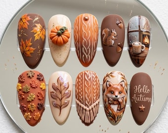 Puede incluir: Un juego de diez uñas postizas en forma de almendra con diseños de otoño que incluyen hojas de arce, una calabaza en 3D, patrones de punto trenzado, una ardilla, una escena de ventana, un zorro y el texto Hello Autumn en blanco.