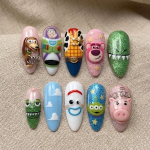 May include: A set of ten press-on nails featuring various character designs from the Toy Story franchise, including Slinky Dog, Buzz Lightyear, Woody, Lotso, Rex, Forky, the Alien, and Hamm, rendered in colorful 3D relief and glitter finishes.