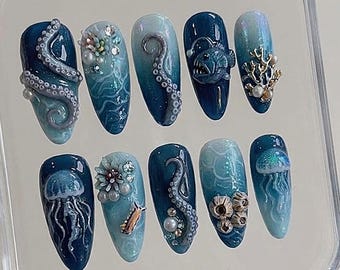 May include: A set of ten press-on nails featuring an ocean theme with deep blue and teal gradients. Designs include 3D octopus tentacles, a glowing anglerfish, jellyfish, coral, barnacles, and small pearls set against swirling water patterns.