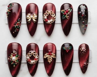 Bordeauxrode kerstnagels, rode fluwelen cat eye nagels, gouden strik-krans nagelkunst, elegante feestelijke nagels, kerstmanicure