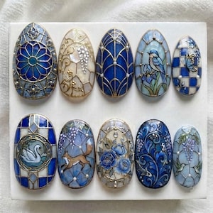 May include: A set of ten oval-shaped decorative plaques featuring intricate stained glass-style designs in shades of blue, white, and gold. The motifs include a swan, a fox, a bird, flowers, butterflies, and hummingbirds, all accented with small white pearls.