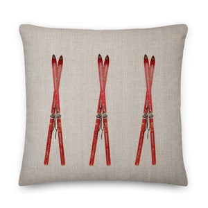 May include: Square throw pillow featuring three pairs of vintage red skis arranged in a crossed pattern. The skis have a distressed appearance with metal bindings. The pillow has a neutral linen-like texture, suitable for a ski lodge or winter-themed decor.