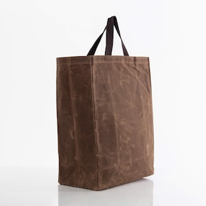 May include: A brown waxed canvas tote bag with dark brown handles. The bag is rectangular with a structured shape and a simple design. The handles are attached at the top and are made of a sturdy material.