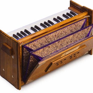 Pode incluir: Um harm&oacute;nio de madeira com um teclado de teclas brancas e pretas. O instrumento tem um exterior castanho com pain&eacute;is decorativos e acabamentos roxos. O fole est&aacute; parcialmente aberto, revelando a estrutura interna.