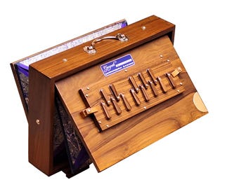May include: A wooden harmonium with a brown finish and a blue label that reads "Gayatri Instruments". The harmonium has a set of brass keys and a leather strap.