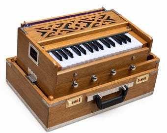 May include: A wooden harmonium with a keyboard, silver accents, and a black handle. The instrument has a decorative top with carved patterns and a small metal plate with the text "Tossie". The harmonium is a musical instrument.