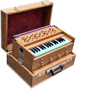 May include: A wooden harmonium with a light brown finish and a green keyboard. The harmonium is open and has a purple and white fabric lining inside. The harmonium is in a wooden case with a handle and metal clasps.