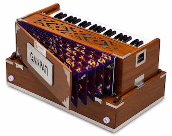 May include: A wooden harmonium musical instrument featuring a keyboard with black and white keys, a bellows system with purple fabric panels, and a silver metal nameplate on the front with the text GANPATI printed in black capital letters.