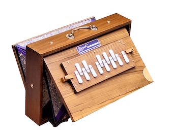 May include: A wooden harmonium with a brown finish and a purple lining. The harmonium has a brass handle and a row of white keys.