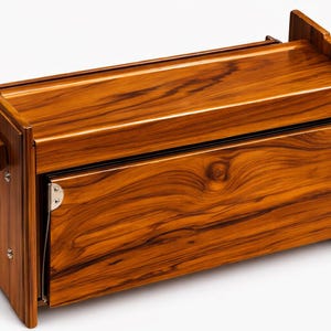 Pode incluir: Uma caixa de madeira com um acabamento castanho quente e um padr&atilde;o proeminente de gr&atilde;o de madeira. A caixa tem um painel frontal articulado e ferragens met&aacute;licas. O design apresenta uma forma retangular.