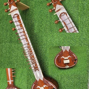 May include: A brown sitar with intricate carvings and a long neck. The instrument features a rounded body and a series of strings. The sitar is decorated with white and silver accents. The sitar is displayed on a green surface.