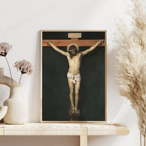 Op de afbeelding: Een ingelijst schilderij dat een religieuze sc&egrave;ne van Jezus Christus aan het kruis afbeeldt. Het schilderij is tegen een donkere achtergrond geplaatst met een houten kruis en een doornenkroon.