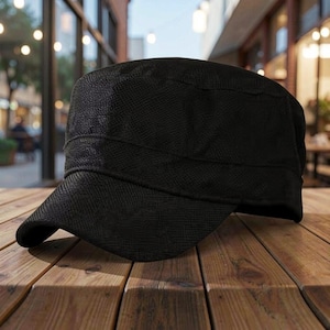 May include: A solid black military-style cadet cap featuring a flat top, a short curved brim, and a textured fabric finish. The hat has a structured crown and a wide band encircling the base, providing a clean and uniform appearance throughout.