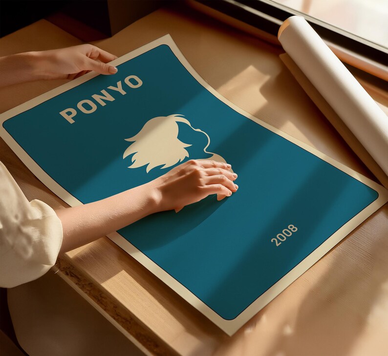 Puede incluir: Un p&oacute;ster turquesa con la palabra "PONYO" en blanco, una silueta blanca de un personaje y el a&ntilde;o "2008". Una persona sostiene el p&oacute;ster. El p&oacute;ster est&aacute; sobre una superficie de madera.