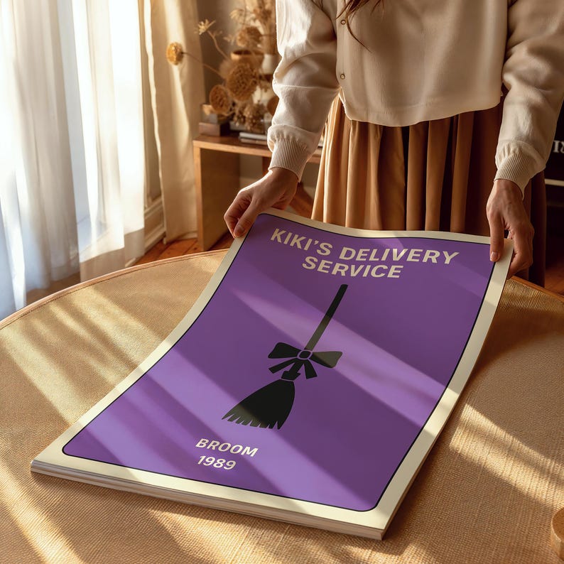 Puede incluir: Un p&oacute;ster con el texto "KIKI'S DELIVERY SERVICE" y una ilustraci&oacute;n de escoba negra sobre fondo morado. La palabra "BROOM" y el a&ntilde;o "1989" tambi&eacute;n est&aacute;n impresos en el p&oacute;ster. El p&oacute;ster est&aacute; sostenido por una persona.
