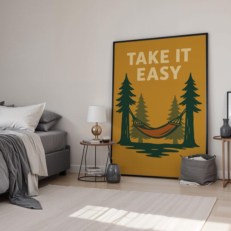 May include: A framed poster with the words "TAKE IT EASY" in white. The poster shows a hammock between green trees, set against a yellow-orange backdrop. The poster is in a bedroom setting, with a bed and side tables.