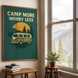 May include: A framed poster with the text "CAMP MORE WORRY LESS" above an illustration of a vintage camper van, sun, and trees. The poster has a dark green background and a wooden frame. The image evokes a sense of adventure and the outdoors.