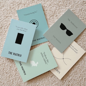 May include: Five rectangular cards featuring quotes and graphics from "The Matrix". The cards are in shades of blue and beige, with text and minimalist illustrations such as sunglasses and a rabbit. Each card has "THE MATRIX" printed on it.