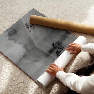May include: A person is rolling up a black and white poster with the text "What are you looking at?" printed on it. The poster features a security camera.