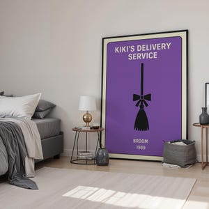 Puede incluir: Un p&oacute;ster enmarcado con fondo morado muestra el texto "KIKI'S DELIVERY SERVICE" y una ilustraci&oacute;n de escoba negra. Las palabras "BROOM 1989" est&aacute;n debajo de la escoba. El p&oacute;ster est&aacute; en un dormitorio con una cama, mesitas de noche y una alfombra.