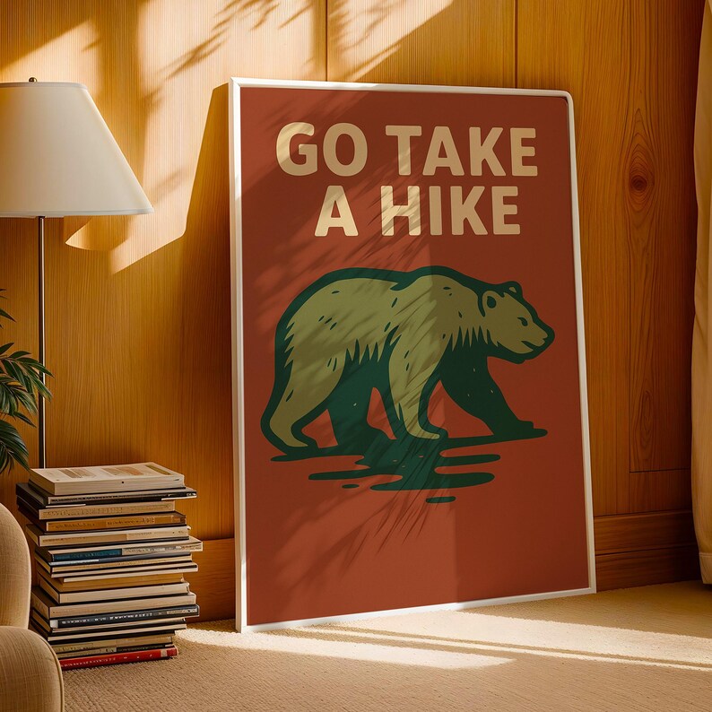 May include: A framed poster with the text "GO TAKE A HIKE" in cream-coloured letters above a green and brown bear illustration. The poster has a red background and a white frame, suitable for home decor.