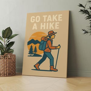 May include: Tan canvas art print with the words "GO TAKE A HIKE" above an illustration of a hiker with a backpack, walking stick, and hat. The background features a sunset, mountains, and pine trees.