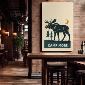 May include: A rectangular canvas print featuring a stylized moose illustration in navy blue and gold against a cream background. Two green pine trees and a gold crescent moon are also depicted. The text "CAMP MORE" is displayed in a navy blue banner.