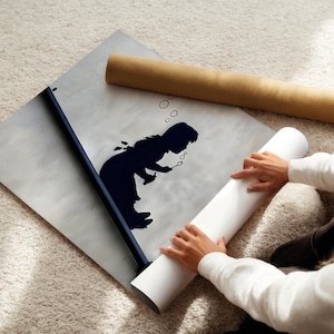 Könnte beinhalten: Eine schwarz-weiße Silhouette eines Kindes, das Seifenblasen auf einem weißen Plakat bläst. Das Plakat wird von den Händen einer Person aufgerollt.
