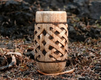 May include: A wooden cup with a carved Celtic knot design. The cup is light brown and has a smooth, polished finish.
