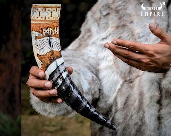May include: A carved drinking horn with a black and white base and a brown and white top. The horn is decorated with a bird and runes. The text on the horn reads "MORK", which is the Norse word for "fate".
