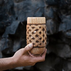 May include: A wooden cup with a carved Celtic knot design. The cup is brown and has a natural wood finish.