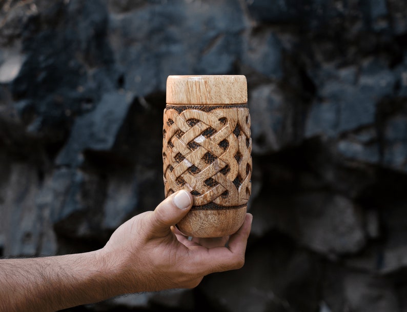 May include: A wooden cup with a carved Celtic knot design. The cup is brown and has a natural wood finish.