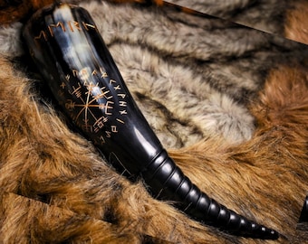 May include: A polished black drinking horn featuring a carved Vegvisir symbol and runic inscriptions in a light gold tone. The horn has a smooth, wide opening that tapers down to a narrow, ribbed, and curved tip with a glossy finish.
