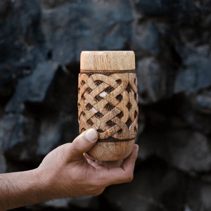 May include: A wooden cup with a carved Celtic knot design. The cup is brown and has a natural wood finish.