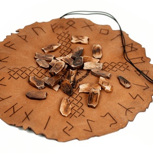 Pu&ograve; includere: Una borsa in pelle marrone con chiusura a cordoncino, contenente un set di rune in legno. Le rune sono sparse sulla borsa, che &egrave; decorata con un cerchio di rune nordiche.