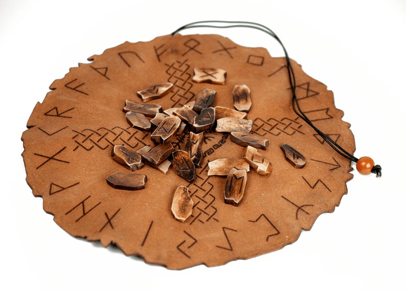 Pu&ograve; includere: Una borsa in pelle marrone con chiusura a cordoncino, contenente un set di rune in legno. Le rune sono sparse sulla borsa, che &egrave; decorata con un cerchio di rune nordiche.